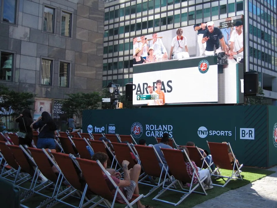 People lounging in front of a giant livestream of the French Open