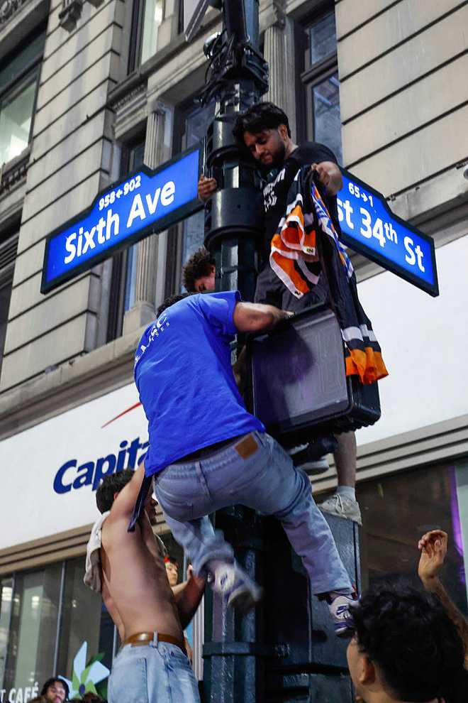 BASKET-NBA-FINALS-GAME 5-FANS Knicks fans climb up a pole as they celebrate after the New York Knicks defeated the San Antonio Spurs in Game 5 of the NBA Finals to win the series, in New York, on June 14, 2026. The Knicks won the NBA Championship for the first time since 1973, for the third time in franchise history. (Photo by kena betancur / AFP via Getty Images)