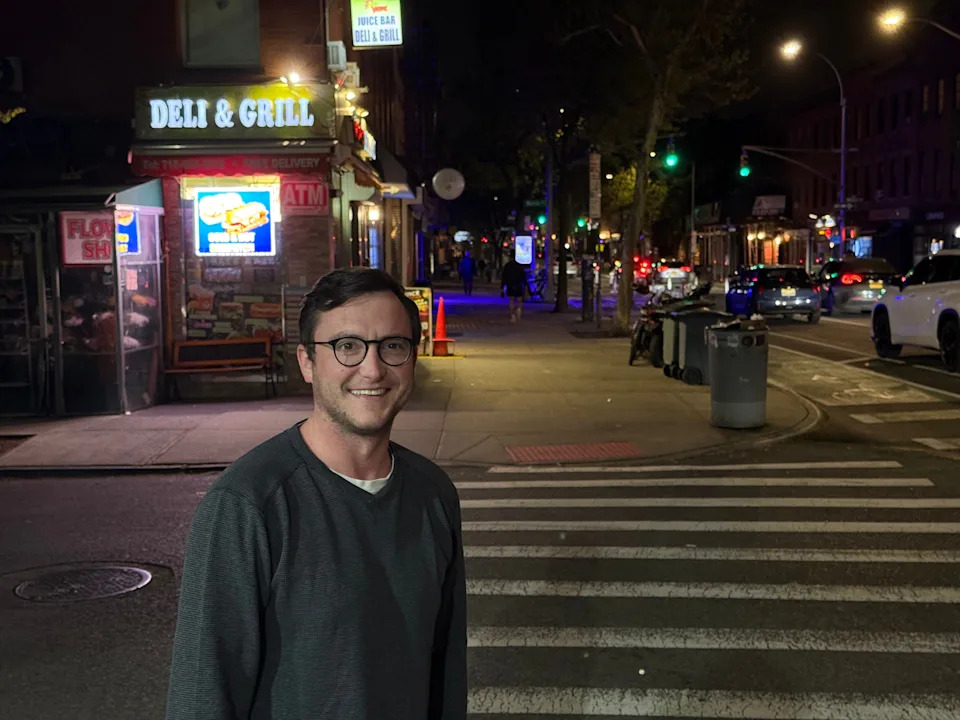 Man standing in New York City near a deli at night