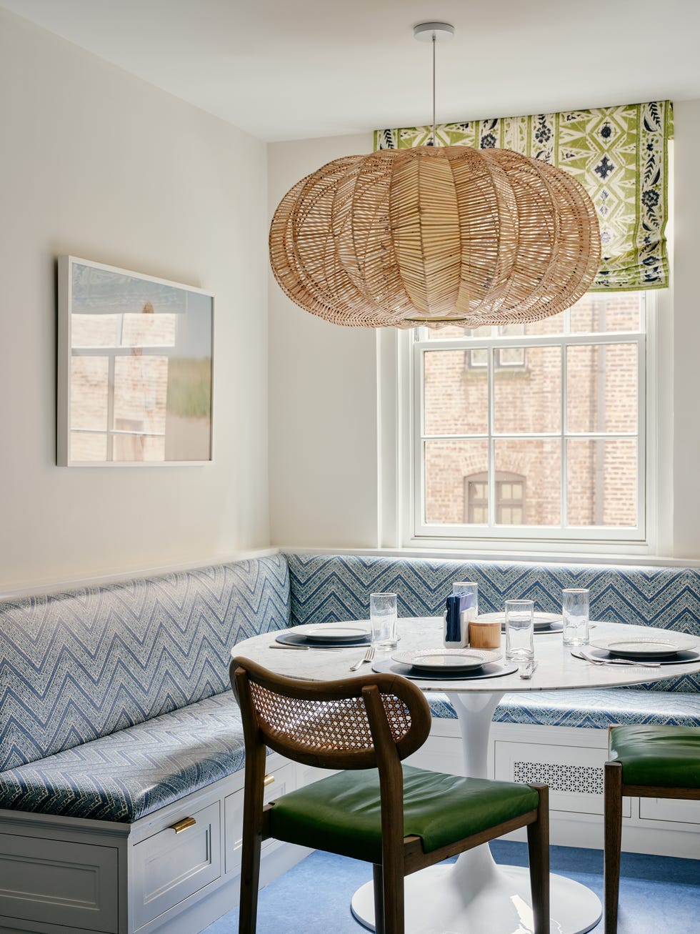 Dining nook with blue patterned bench, white table, wooden chairs, and woven light fixture.