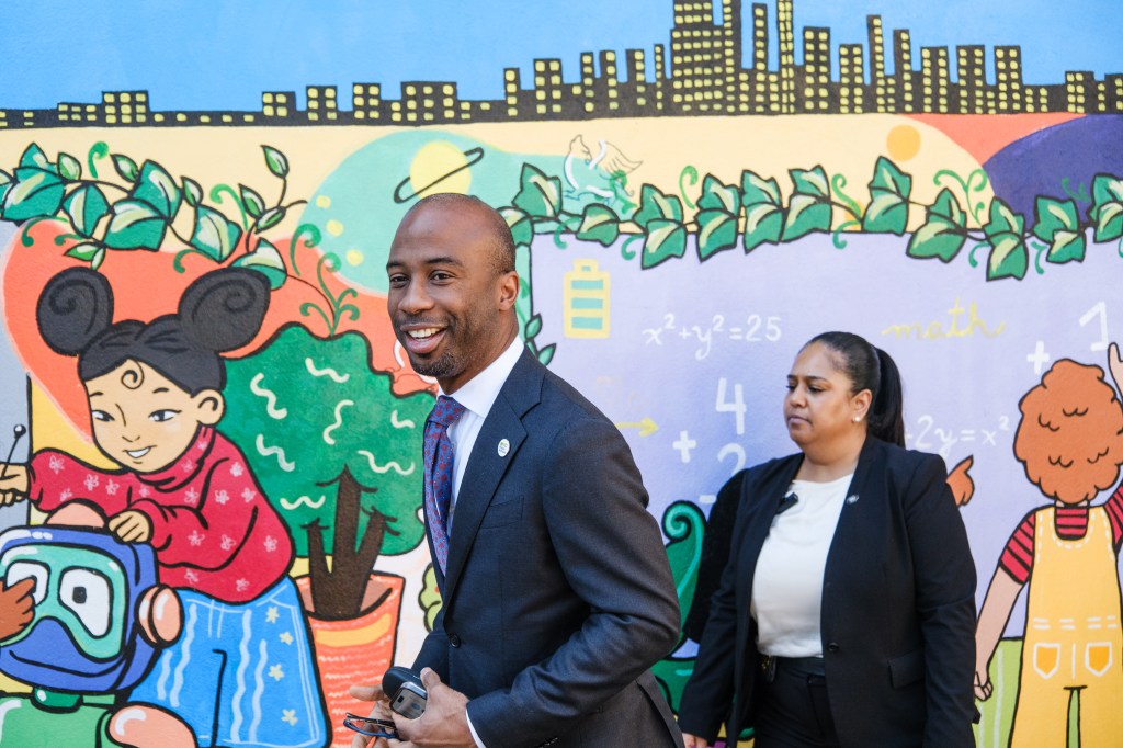 DOE Chancellor Kamar Samuels smiling and walking past a colorful mural.