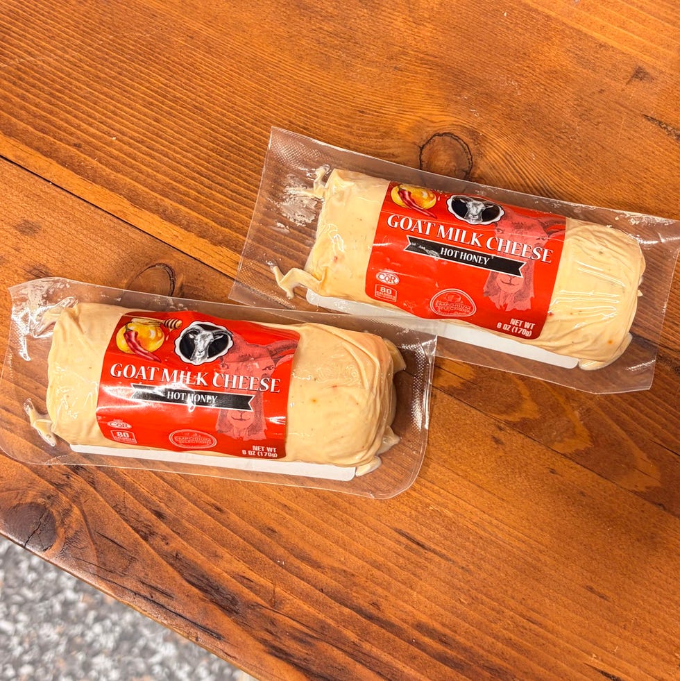 Two packaged hot honey goat cheese logs on a wooden table with a sign.