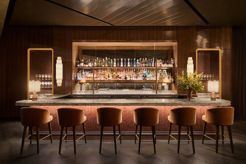 Elegant bar with plush stools, marble counter, and illuminated shelves of bottles.
