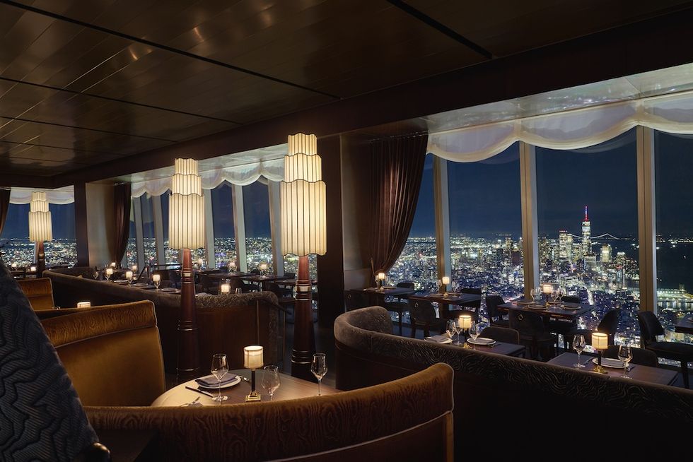 Elegant restaurant with night city skyline view through tall windows.