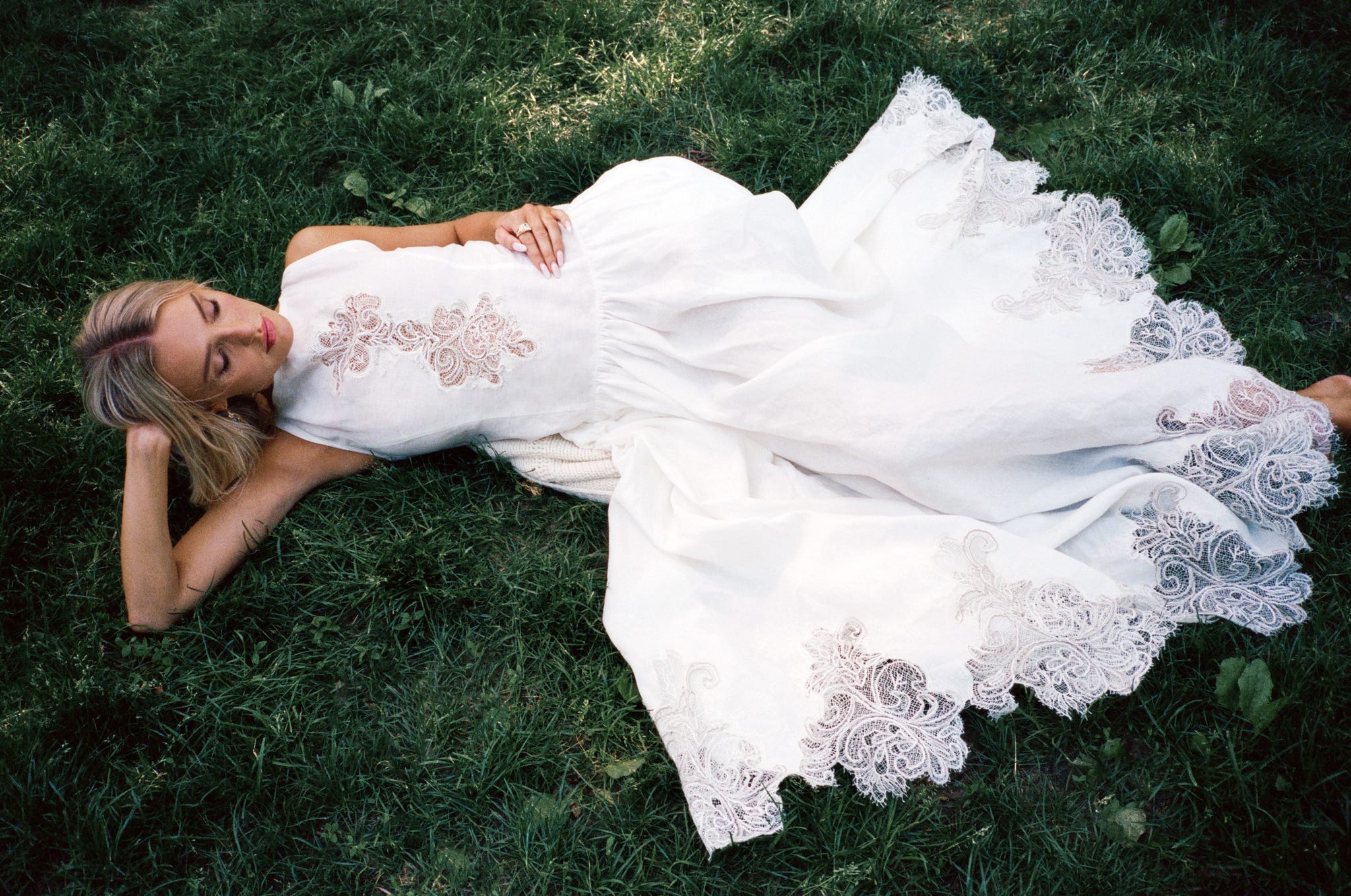 Person in white dress with lace details lying on grass.