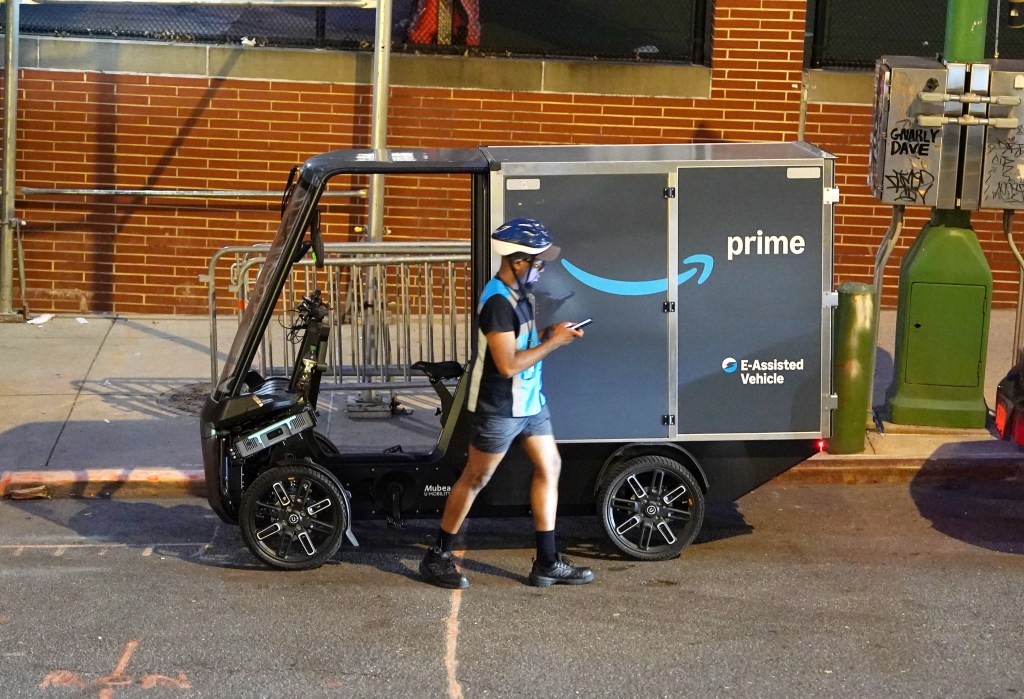 An Amazon Prime delivery driver looks at their phone next to an Amazon Mubea U-Mobility E-Cargobike.