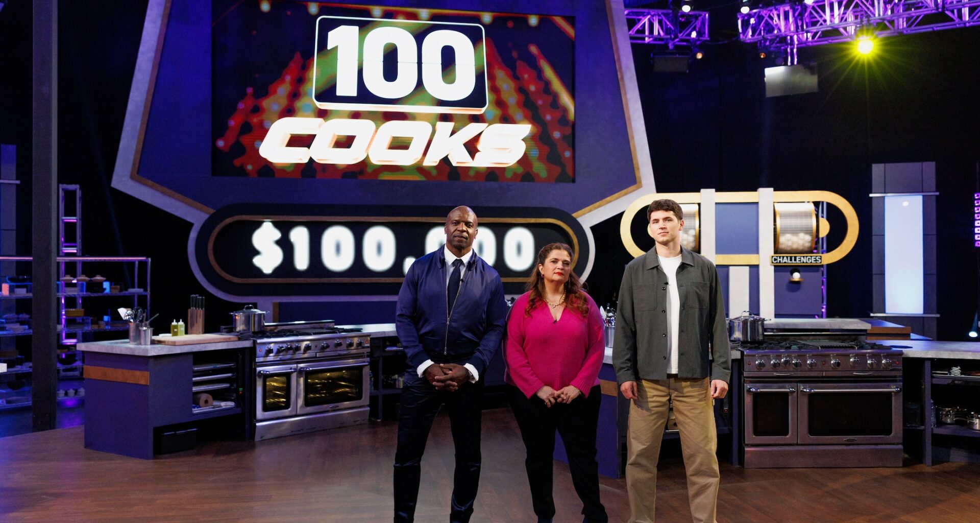 Host Terry Crews with Judges Alex Guarnaschelli and Nick DiGiovanni posed in front of LED board, as seen on 100 Cooks, Season 1.