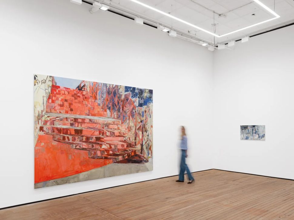 An installation view shows a large red and pink abstract painting on the left wall, a smaller blue-toned painting on the far wall and a blurred visitor walking through the white gallery space.
