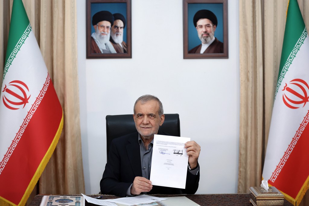 Iranian President Masoud Pezeshkian holding up a signed memorandum of understanding.