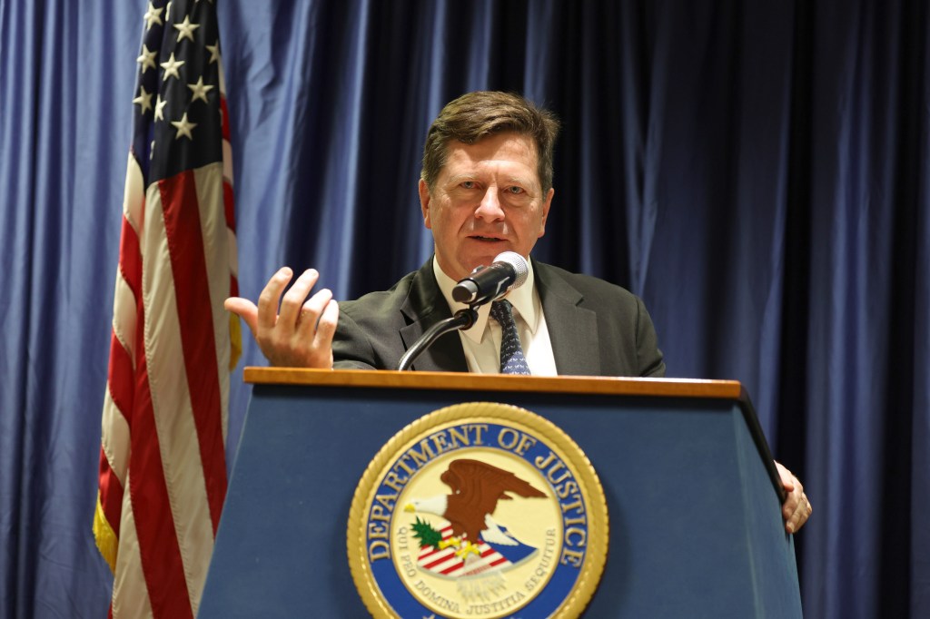 Jay Clayton speaks at a podium with a Department of Justice seal, next to an American flag.