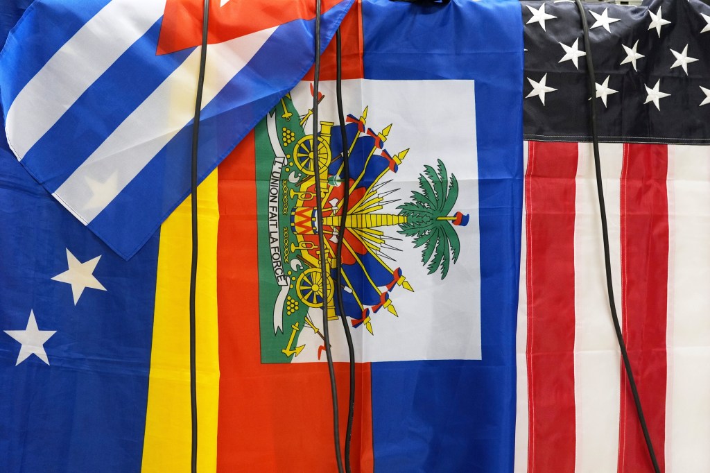Flags of Cuba, Venezuela, Haiti, and the United States, with microphone cables hanging over them.