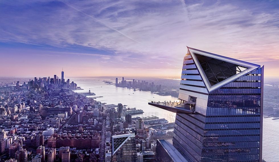 Modern skyscraper with triangular rooftop at sunset, overlooking a city and river view.