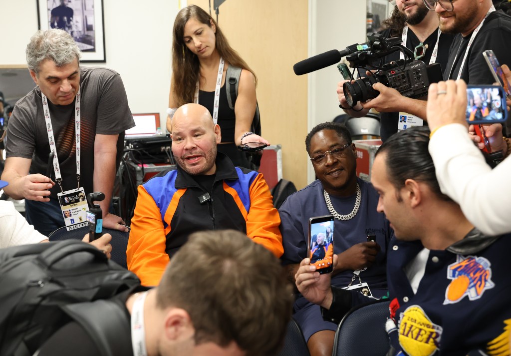 Rapper Fat Joe in a blue jacket and a black New York Knicks hat, yelling courtside at an NBA Finals game.