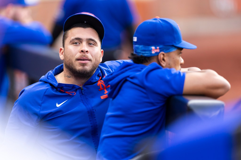 New York Mets player Francisco Alvarez in the dugout wearing a blue hoodie and cap.