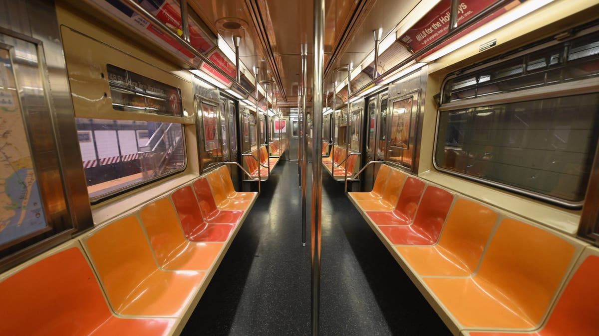 An empty New York subway car interior with rows of seats and handrails.