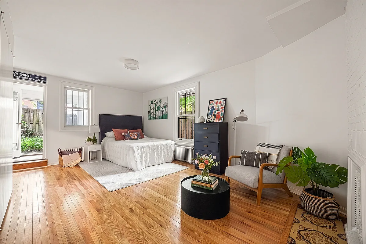 bedroom with wood floor, white walls, door to rear yard