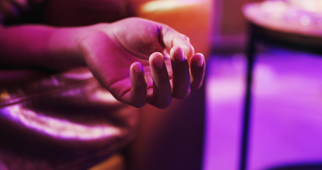 Closeup of a person's hand under neon light at a house party, conveying low energy or an overdose.