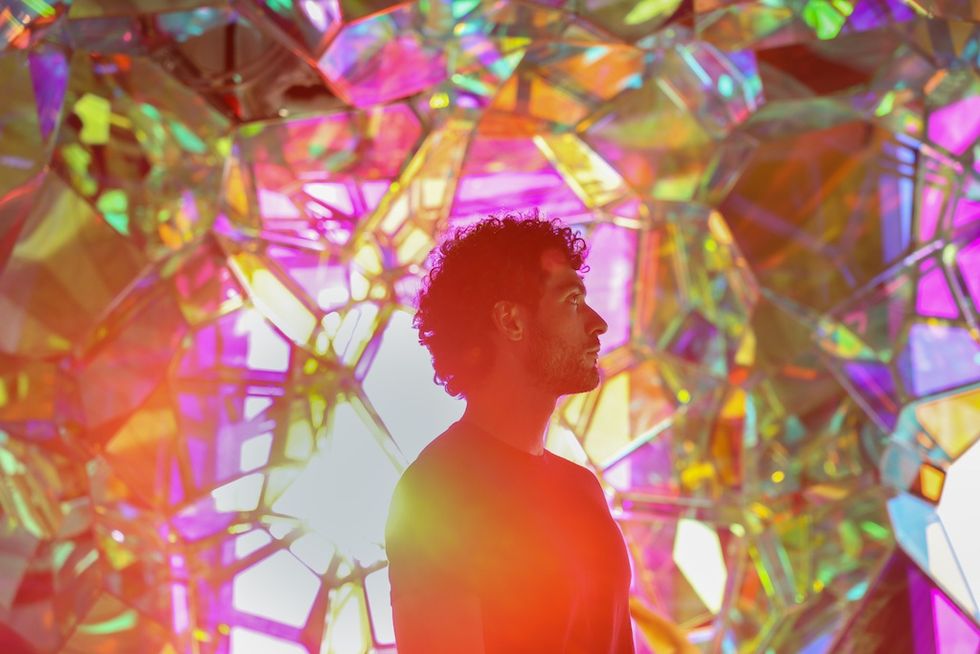 Person in front of a vibrant, colorful, iridescent background - Crystal Cave at Edge NYC