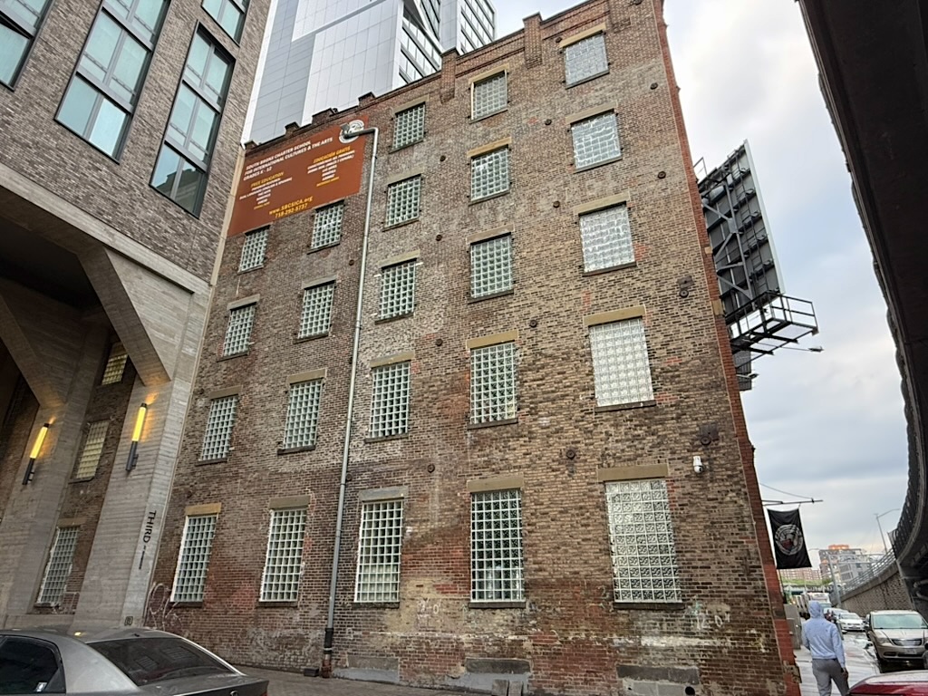 A brick building with glass block windows, located between modern structures in an urban setting.