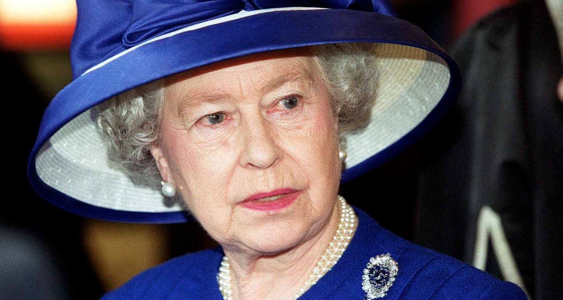 Britain's Queen Elizabeth II during a visit to Fitzalen High School wearing a royal blue suit with a matching wide-brim hat, a pearl necklace, and a sapphire and diamond brooch