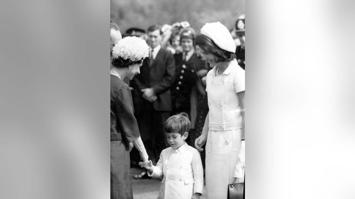Queen Elizabeth II standing with John Kennedy Jr. and Jackie Kennedy at a memorial inauguration.