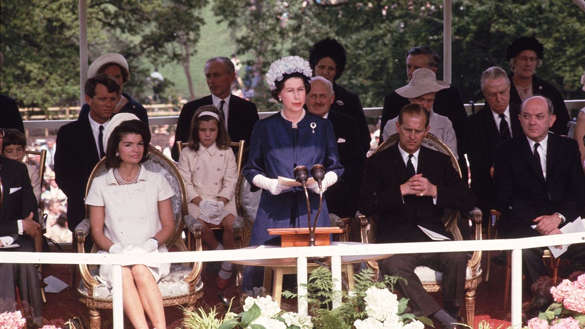 Queen Elizabeth II and Prince Philip standing with Jackie Kennedy and her daughter Caroline at Kennedy memorial.