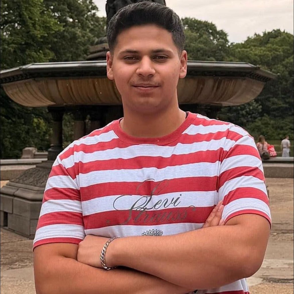 Romanch Mahajan, an 18-year-old, stands with his arms crossed in front of a fountain.