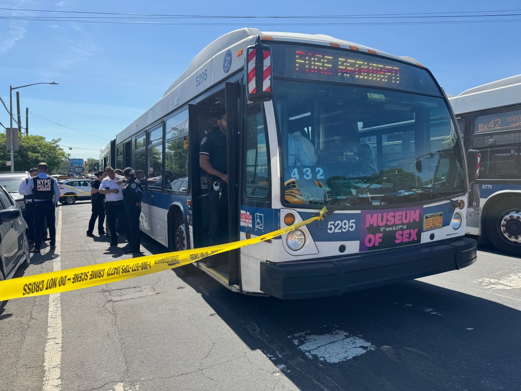 NYPD officers investigate a fatal shooting on board an MTA bus, with crime scene tape across the front of the bus.