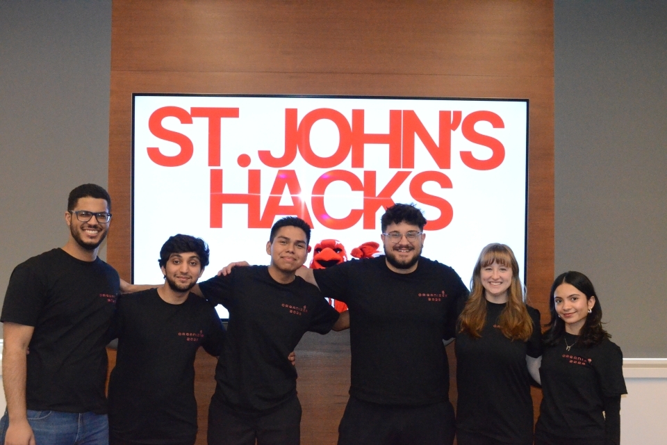 Group of students standing behind a sign in Red that says "St. John's Hacks" 
