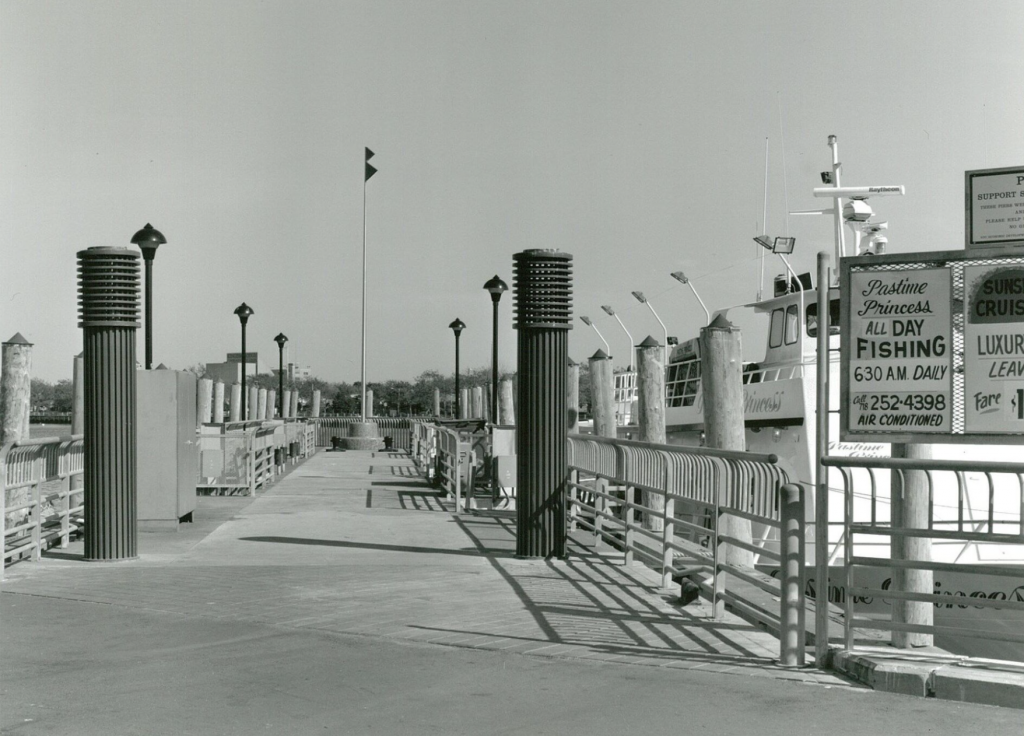 a photograph of a pier with distinctive lampposts and signs for fishing on the right handside.