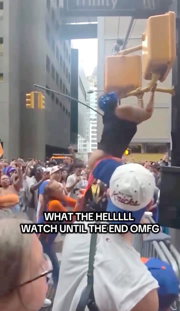 A woman in an orange thong hangs from a traffic light over a crowd at a New York Knicks parade.