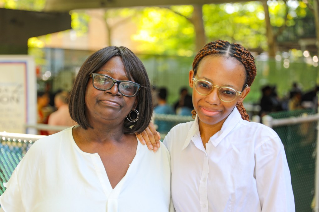 Rochelle and Lillian Williams both wear white button up dress shirts. Rochelle has her hand on her mothers shoulder, leaning slightly towards her.