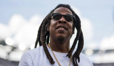 Jay-Z smiles and looks upwards, surrounded by a stadium setting.