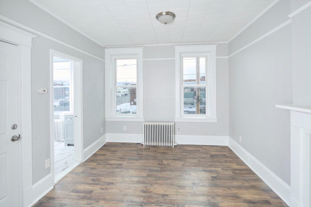 Empty room in a home with wooden floor, white walls and two windows.