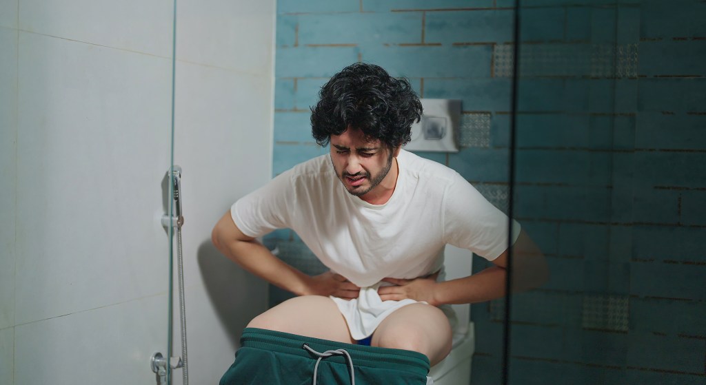 A person suffering from stomach pain on a toilet.