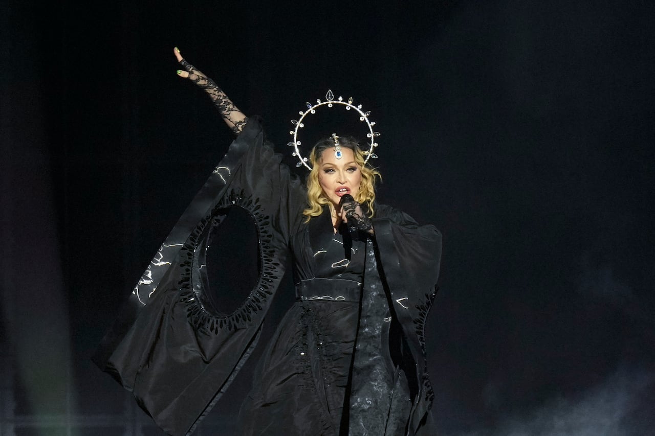 A woman in a black dress and a crown sings into a microphone.