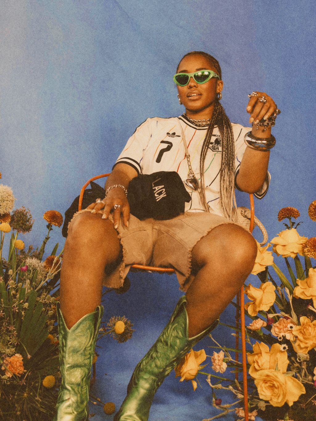 A person wearing sunglasses, a jersey, and cowboy boots sitting in a field of flowers.