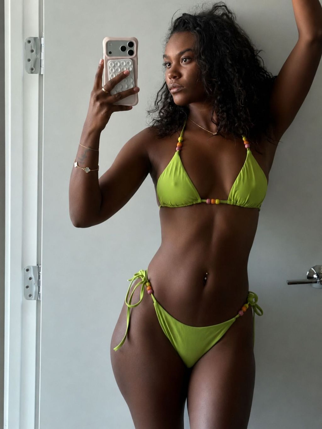 A woman in a neon green bikini taking a selfie in front of a white wall.