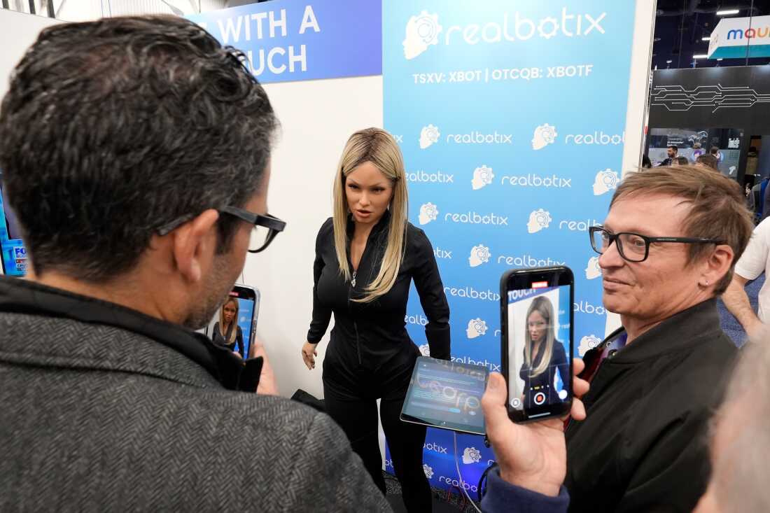 FILE - A Realbotix humanoid robot, center, speaks with attendees at a Realbotix booth during the CES tech show Jan. 8, 2025, in Las Vegas.