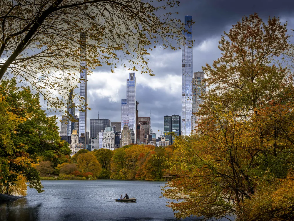 OPENER - Autumn colors frame a calm lake in Central Park as two people row beneath looming skyscrapers.