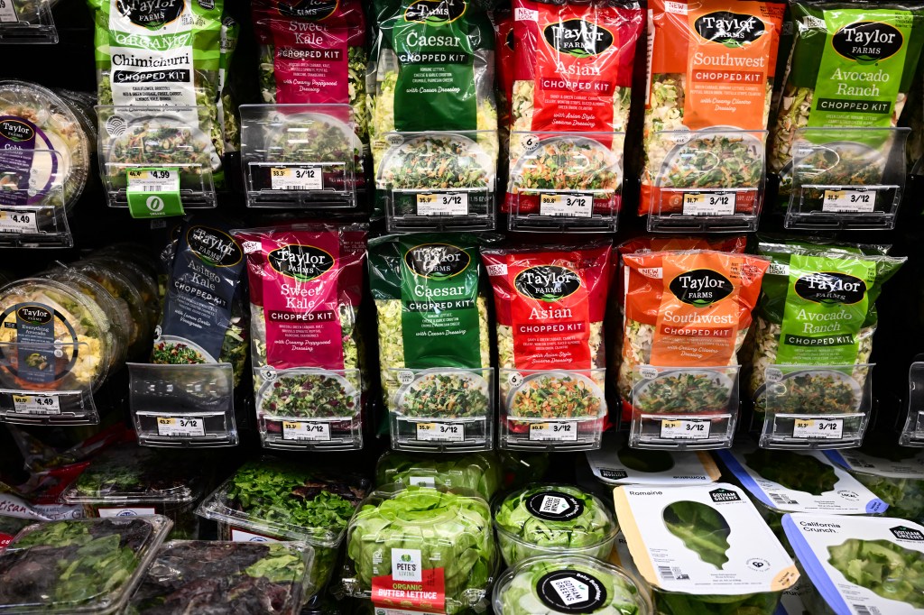 Packages of Taylor Farms salad kits and fresh lettuce for sale in a grocery store.
