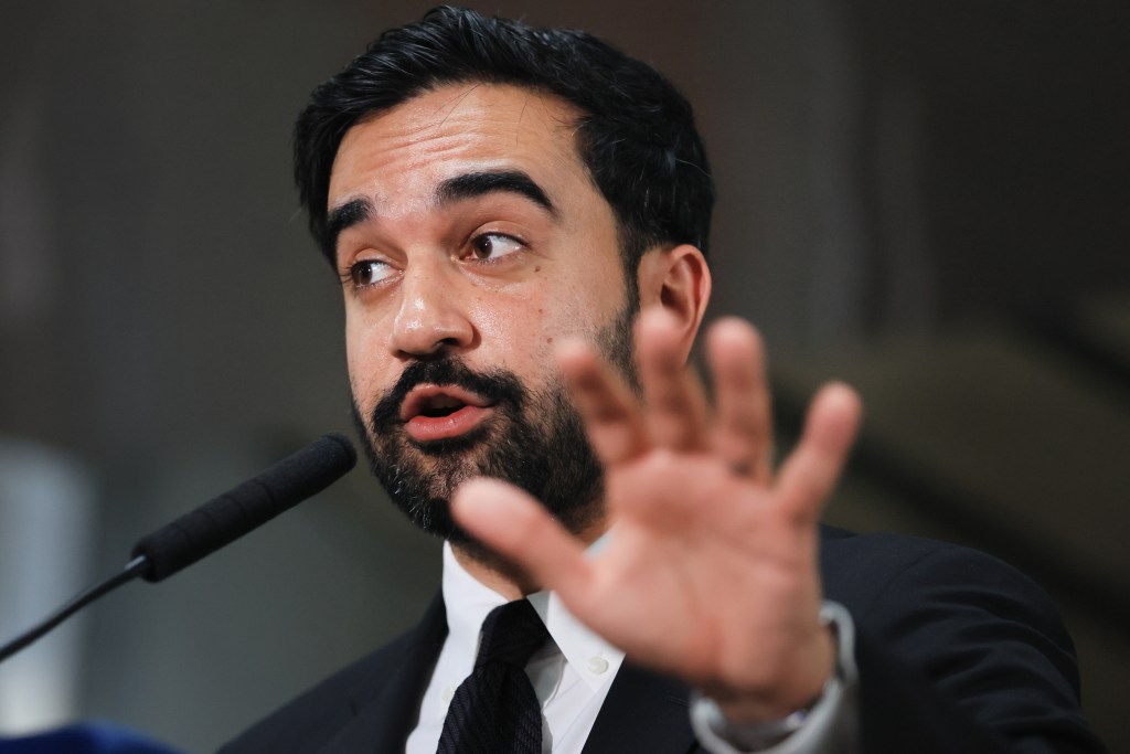 NYC Mayor Zohran Mamdani speaks at a news conference, with his right hand extended forward.