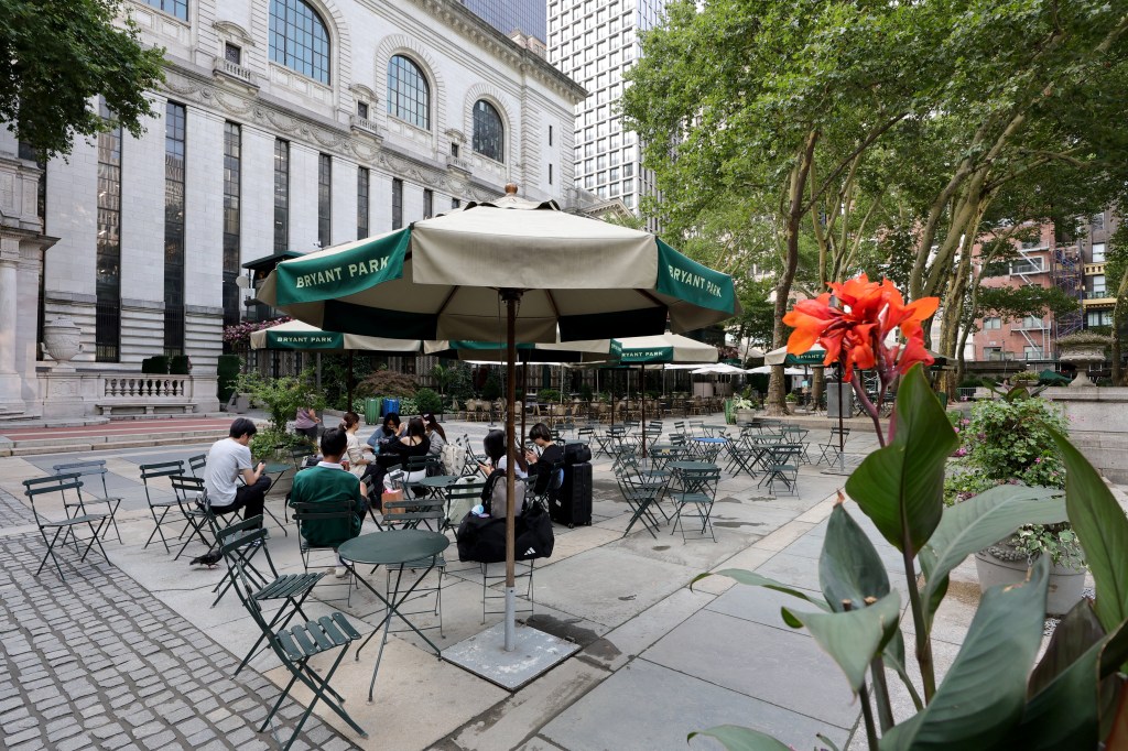 A partial view of Bryant Park, with people dining outdoors under green and white umbrellas.