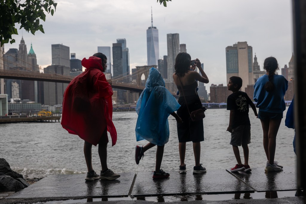 People in rain ponchos look at the New York City skyline from Dumbo, Brooklyn.