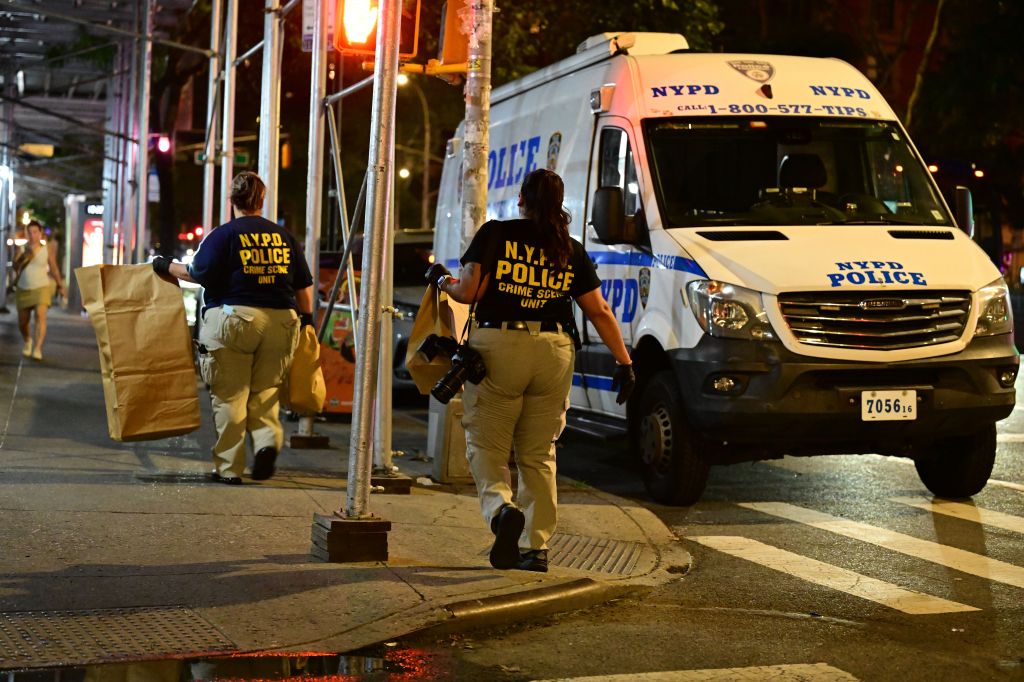 NYPD Crime Scene Unit investigators removing evidence bags near a police van in front of the Belnord Hotel.