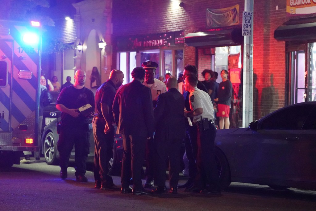 Police gather at the scene of a fatal shooting with an ambulance in the background.