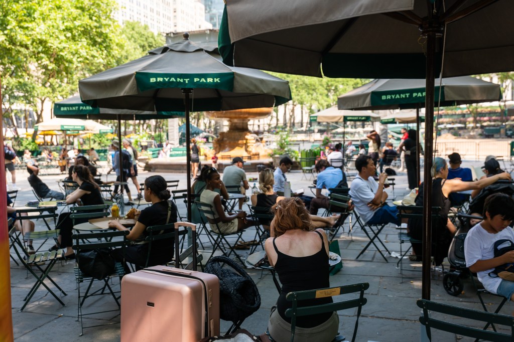 People sit under large green and beige umbrellas in Bryant Park.
