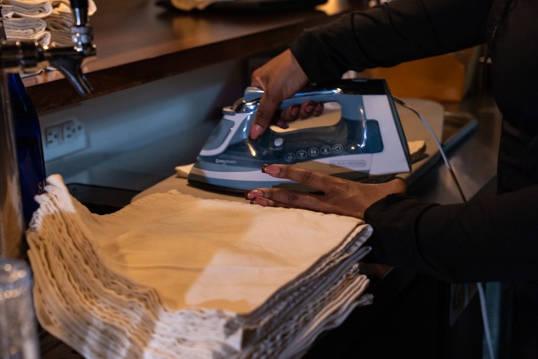 Bar Manager Victoria Legester irons napkins at La Cachette du Coin, 625 Rogers Avenue, Brooklyn, May 14, 2026. Photo by Allison Hunter for The Haitian Times. 
