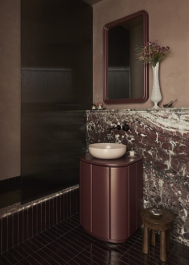 Elegant bathroom with maroon vanity, marble backsplash, large mirror, and decorative vase on the countertop.