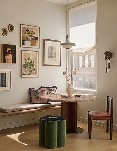 Cozy dining area with art-filled wall, round table, modern chairs, and large window allowing natural light to fill the space.